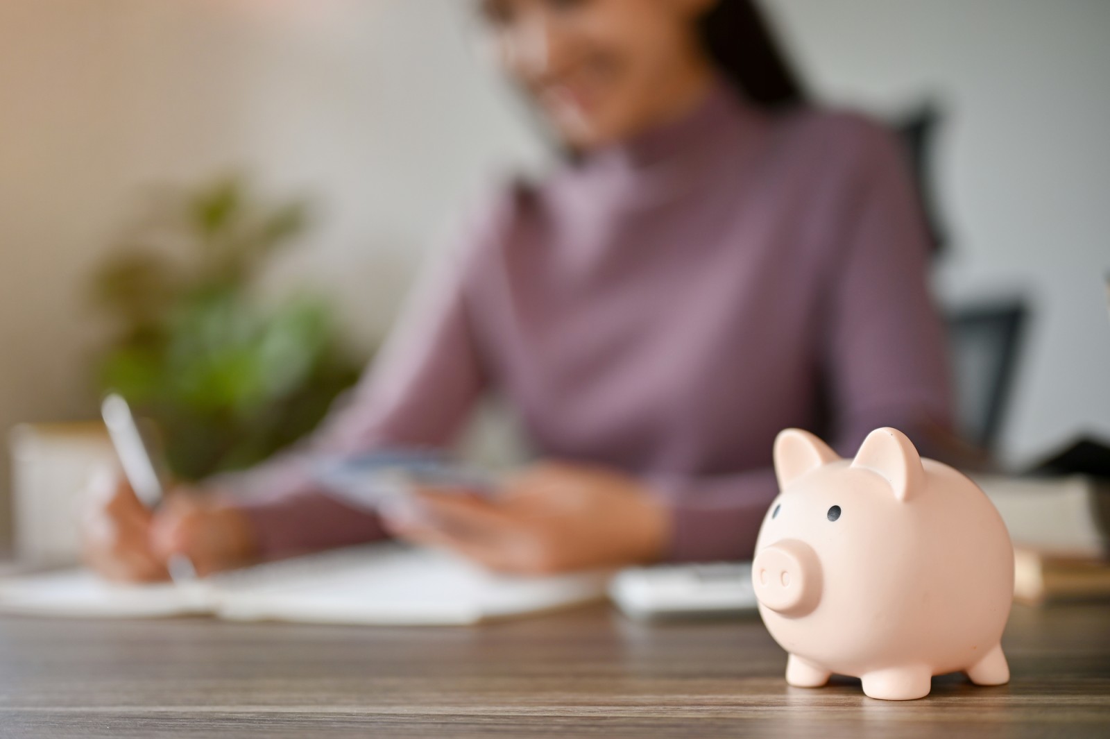 Woman at desk working on budget with pink moneybox in foreground