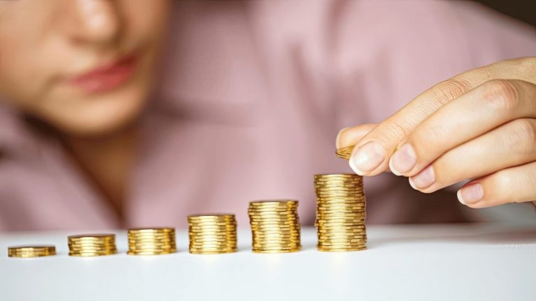 woman adds coins to a growing stack of gold coins, representing financial growth or wealth accumulation