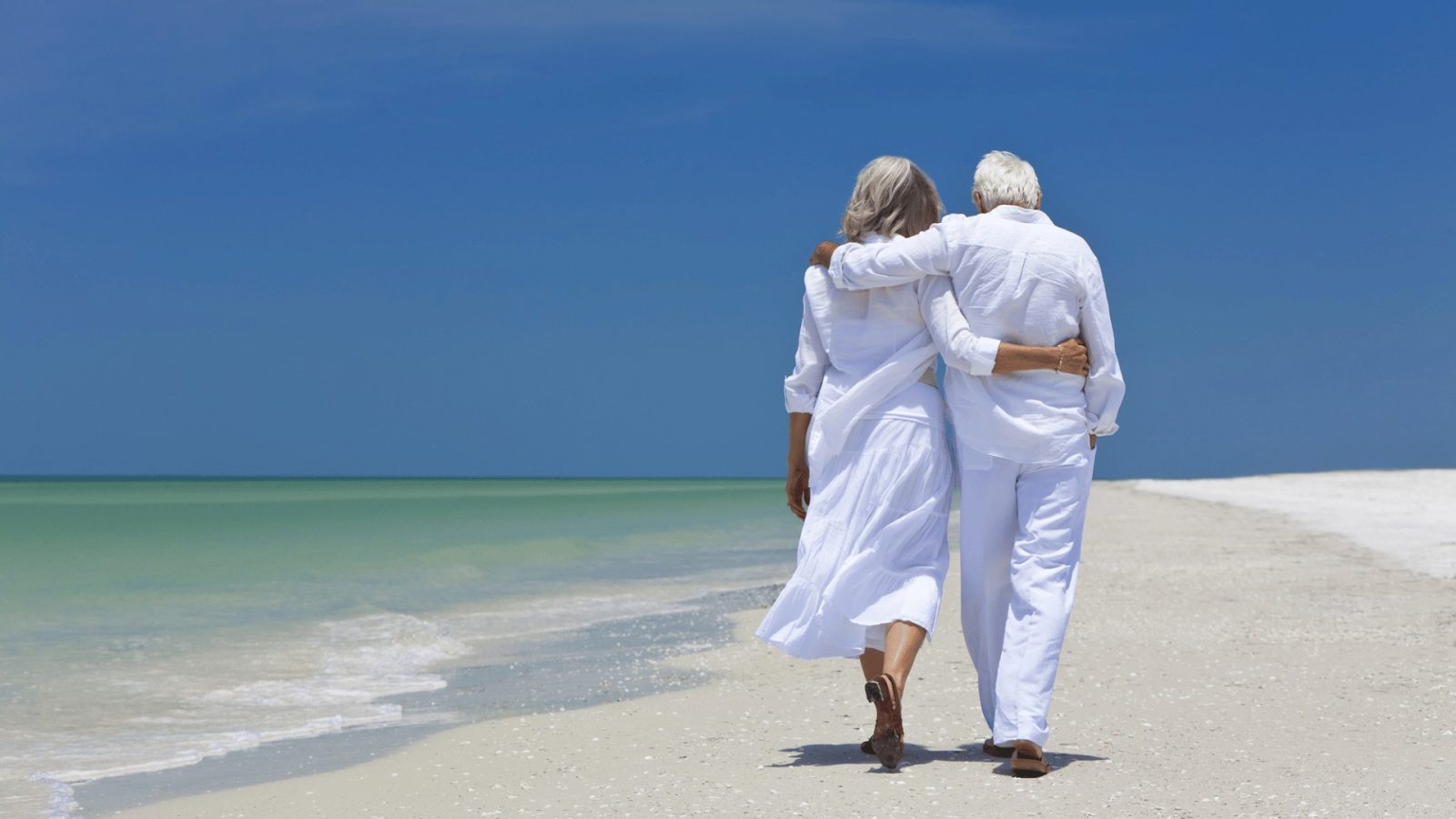 senior man and woman walking together on a beach surrounded by soft sand and the ocean