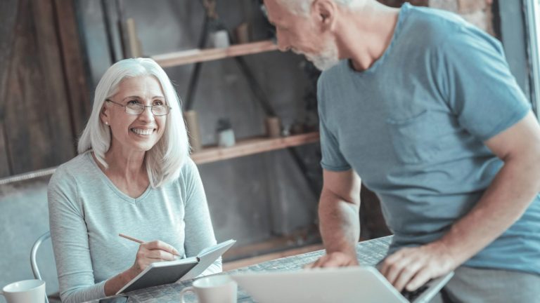 elderly man and woman engaged in discussion while using a laptop at a table
